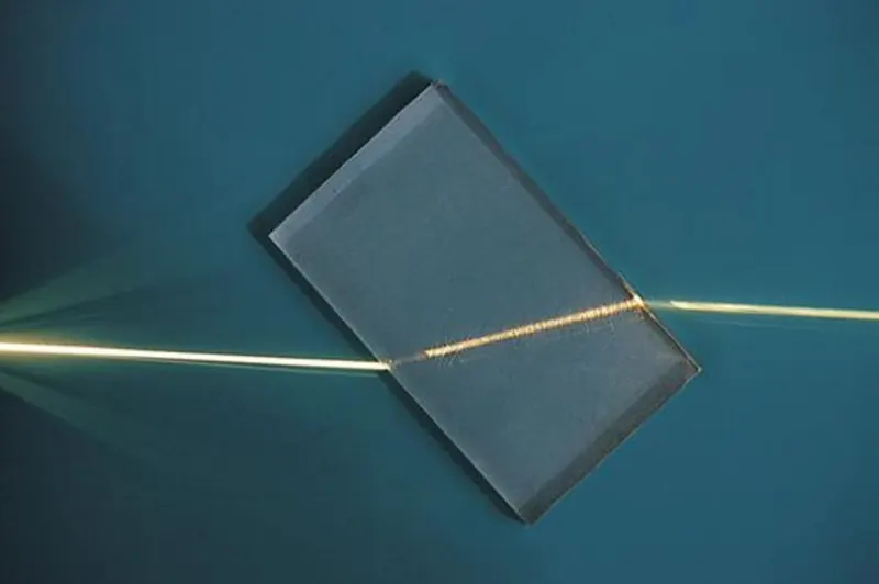 A narrow beam of light passing through a glass block on a table