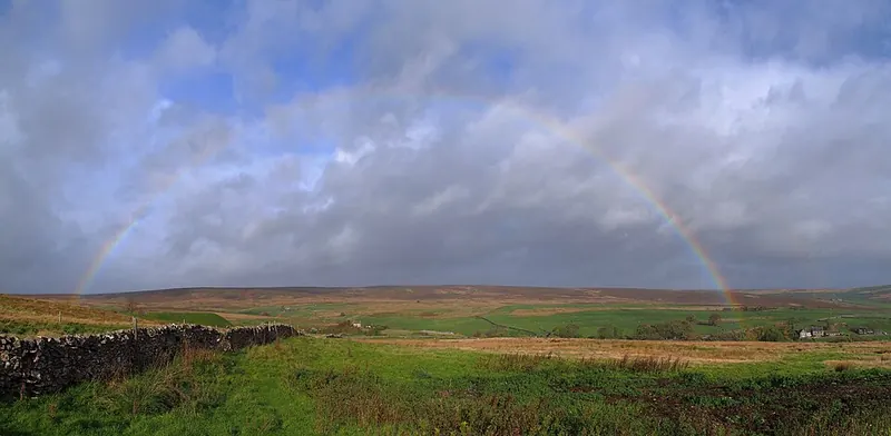 A rainbow arching over green fields under a cloudy sky