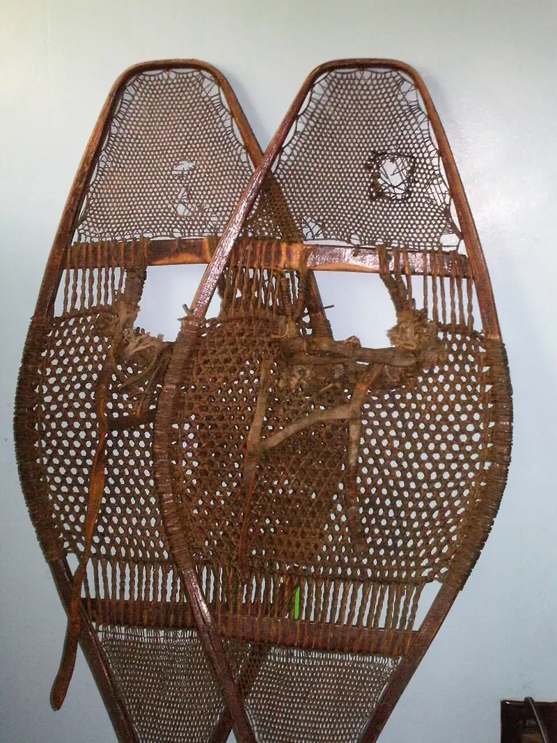 A pair of old wooden snowshoes with woven netting