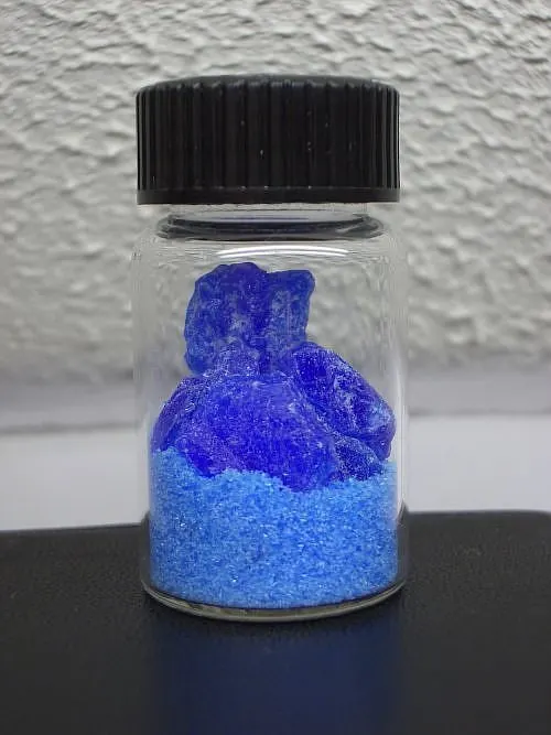 Blue copper sulfate crystals and powder in a small glass jar