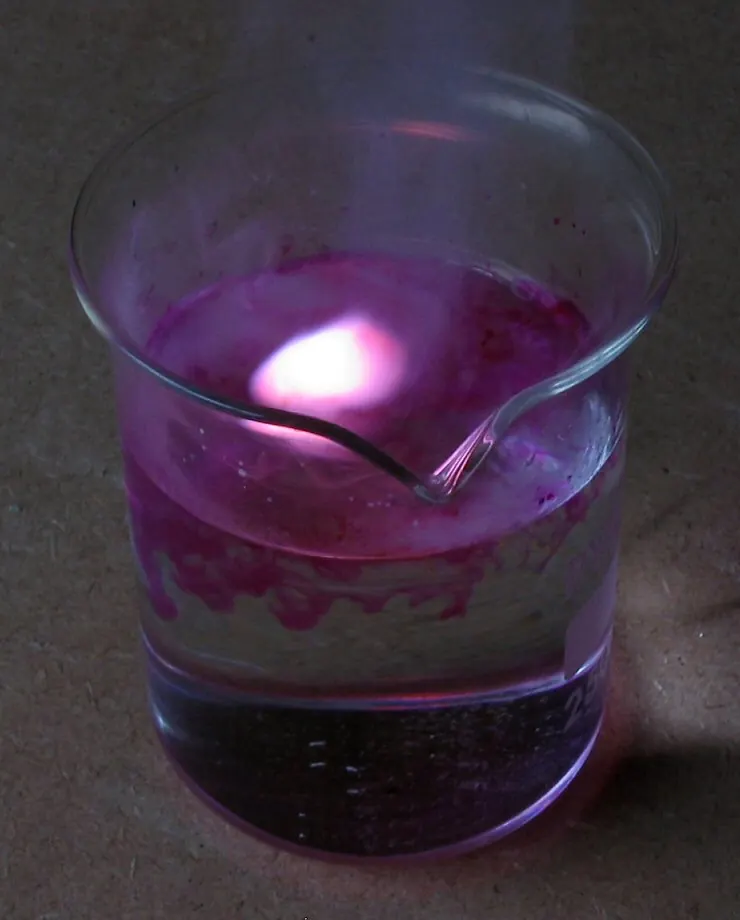 Potassium reacting on water in a beaker with a lilac flame