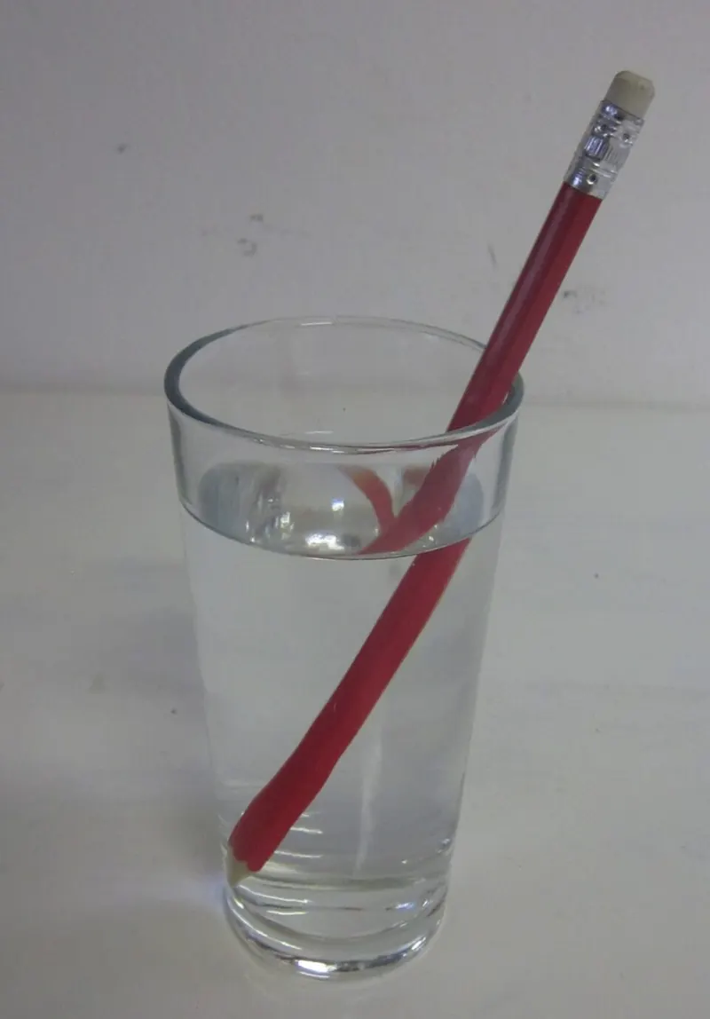 A red pencil standing in a glass of water, looking bent at the water surface